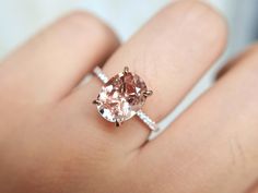 a woman's hand holding an engagement ring with a pink morganite and diamond band