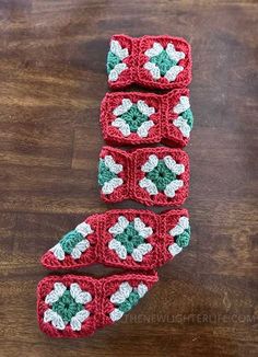 three crocheted red and green squares with white flowers on them sitting on top of a wooden table