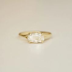 a yellow gold ring with an oval cut diamond in the center, on a white surface