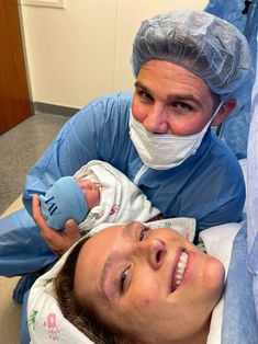 a man holding a baby in a hospital bed while wearing a surgical mask and gown