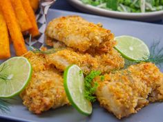 some fried food on a blue plate with limes and carrot sticks next to it