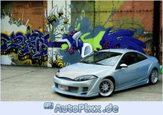 a silver car parked in front of a graffiti covered wall