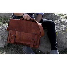 a person sitting on a rock with a brown briefcase in their lap and one hand holding the bag