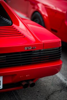 the front end of a red sports car parked in a parking lot next to other cars