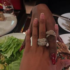 a woman's hand with two rings on her fingers and a salad in the background