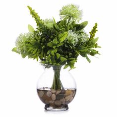 a glass vase filled with lots of green plants and rocks on top of a white surface