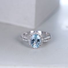 an oval cut blue topazte and diamond ring on a white surface with a box in the background