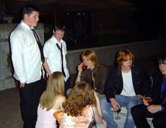 a group of young people sitting around each other on a bench outside at night with drinks in their hands