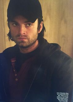 a man with long hair wearing a black hat and looking off to the side while standing in front of a wooden wall