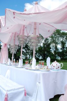 a table set up for a tea party with chandeliers and pink decorations on it