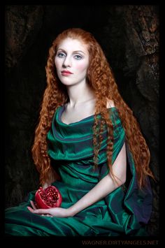 a woman with long red hair wearing a green dress and holding a heart shaped box