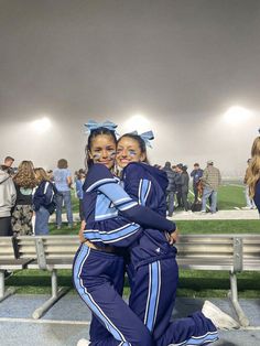 two young women hugging each other while sitting on a bench in the middle of a stadium