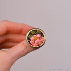 a hand holding a ring with flowers painted on the front and back of it,