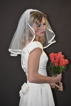 a woman in a white wedding dress holding a bouquet of red roses and wearing a veil