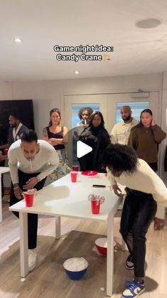 a group of people standing around a table with cups on it and one person bending over