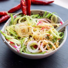 a white bowl filled with vegetables on top of a wooden table next to red peppers