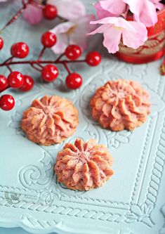 three cookies with icing and cherries sitting on a blue tray next to pink flowers