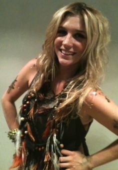 a woman with long hair and tattoos standing in front of a mirror smiling at the camera