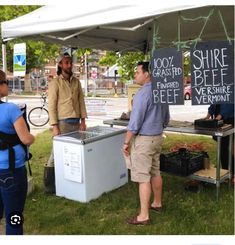 three people standing under a tent with signs on it