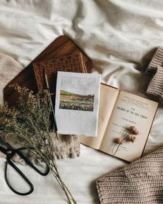 an open book sitting on top of a bed next to flowers