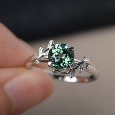 a close up of a person's hand holding a ring with a green stone