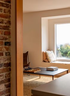 a living room filled with furniture and a large window next to a brick wall on top of a hard wood floor