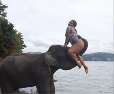 a woman is riding on the back of an elephant in front of a body of water