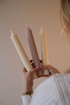 a woman holding three white candles in her hands and looking at the top one with two smaller ones on it