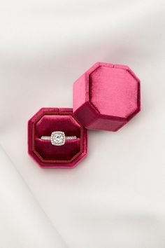 an open pink velvet ring box with a diamond in it on a white cloth background