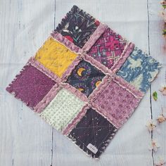 a patchwork piece of cloth on top of a wooden table with flowers in the background