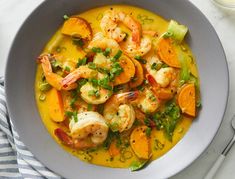 a white bowl filled with shrimp and carrots next to a glass of orange juice