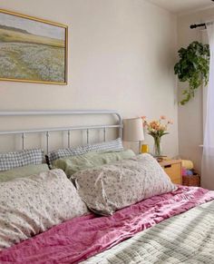 a bed with pink sheets and pillows next to a painting on the wall above it