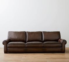 a brown leather couch sitting on top of a hard wood floor next to a white wall