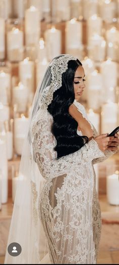 a woman in a wedding dress is looking at her cell phone while standing next to candles