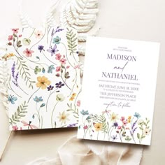 the wedding stationery is laid out on top of white fabric and has flowers painted on it