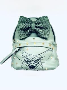 Dark yellowish toned green backpack with green reptile bow and gold studs and spikes with grimlins design measurements: h11 l9 w6.5 Luxury Green Luxury Backpack, Green Reptile, Green Backpack, Studs And Spikes, Green Backpacks, Gold Studs, Reptiles, Purses And Handbags, Shoulder Bags