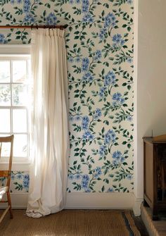 a room with blue flowers on the wall and a chair in front of a window