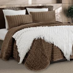 a bed with brown and white comforters on top of it, next to a potted plant