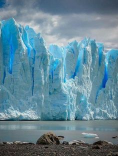 a large iceberg towering over a lake filled with rocks and water under a cloudy sky