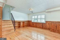 an empty living room with wood paneling and stairs leading up to the second floor