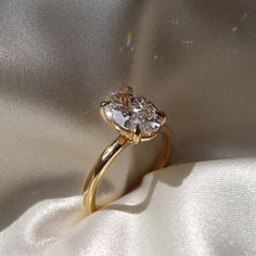 a yellow gold engagement ring with two pear shaped diamonds on it's side, sitting on a white fabric