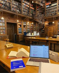 an open laptop computer sitting on top of a wooden table next to bookshelves