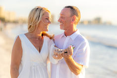 a man and woman standing next to each other on the beach holding wine glasses in their hands