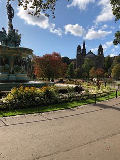 a large fountain in the middle of a park with lots of trees and flowers around it