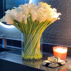 white flowers in a glass vase next to a candle