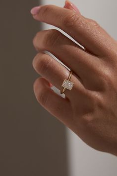 a woman's hand with a diamond ring on top of her finger, in front of a white wall