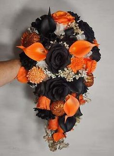 a person is holding a bouquet with orange and black flowers on the bottom half of it