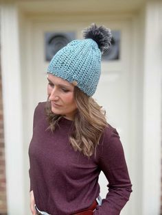 a woman wearing a blue knitted hat with a pom - pom on it