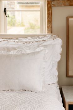 a bed with white sheets and pillows in front of a window