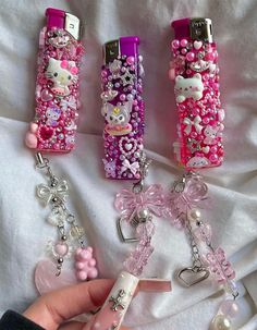 three hello kitty cell phones are shown with key chains attached to them, one is pink and the other is white